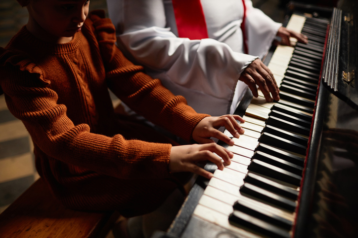 Close-up of woman from the church choir teaching girl to play piano